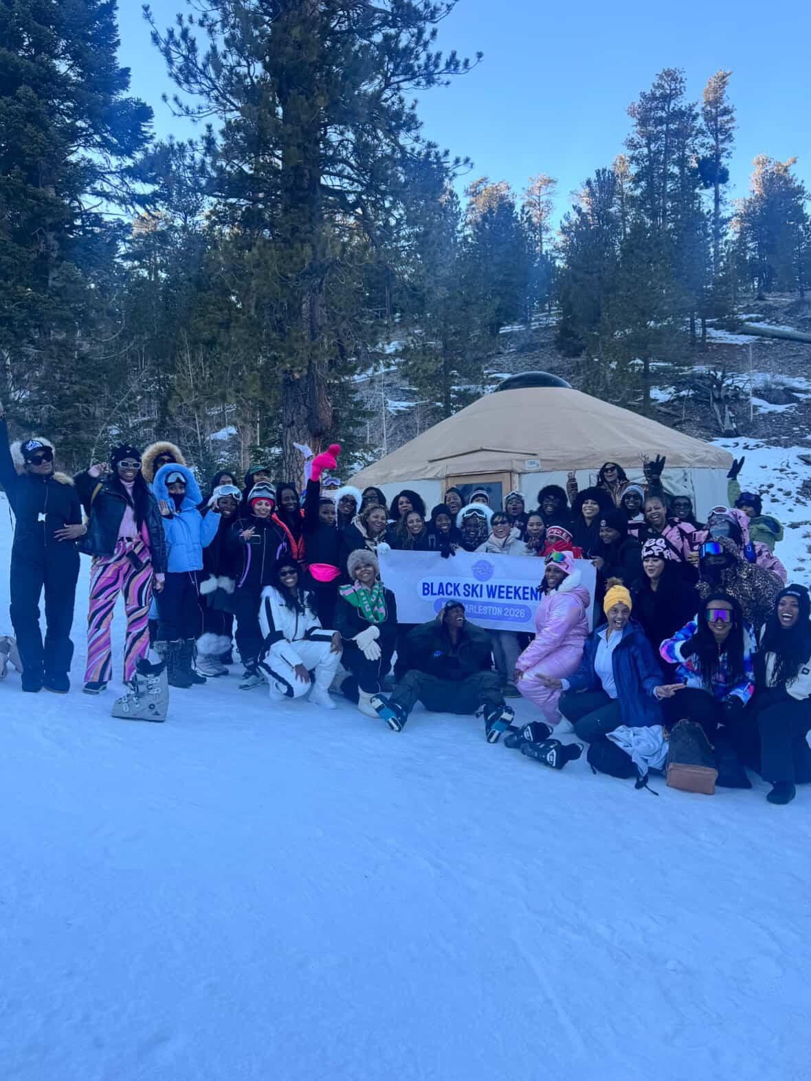 A large group of skiers gathered in the snow for a group photo at a ski weekend event